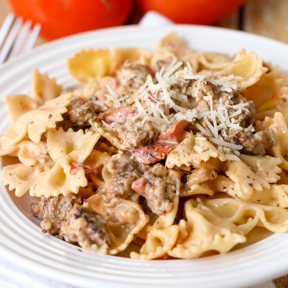 Italian Sausage Pasta on a white plate topped with shredded parmesan.