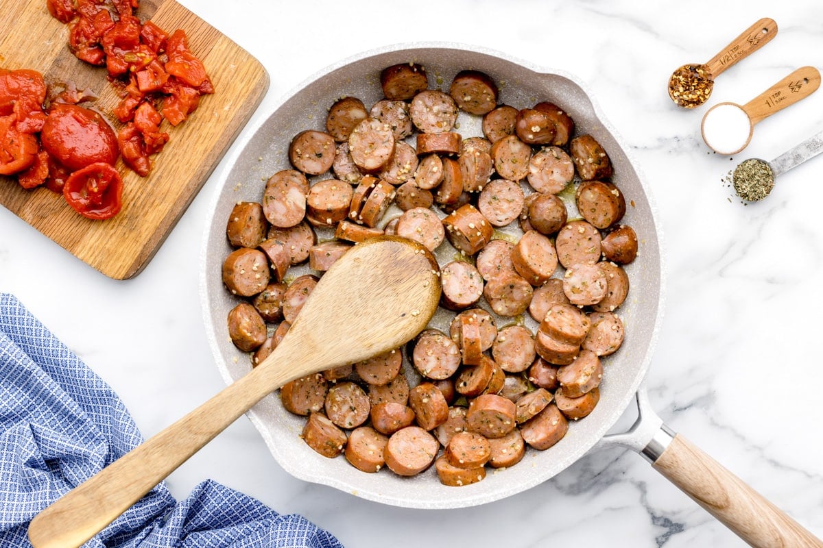 Cooking sausage in a skillet with seasonings.