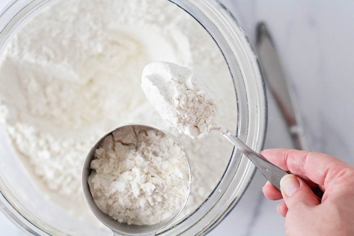 Spooning flour into a measuring up with some flour in it.