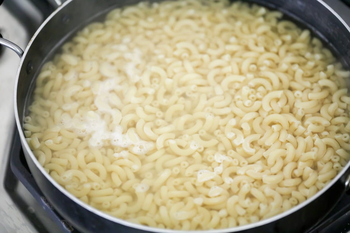 Elbow macaroni cooking in pot with water.